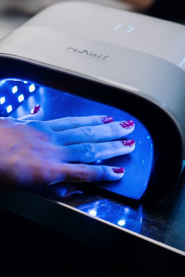 engagements-photography-04 A hand with red nail art curing under a UV lamp in a professional nail salon.